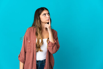 Young caucasian woman isolated on blue background having doubts while looking up