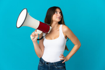 Young caucasian woman isolated on blue background holding a megaphone and thinking