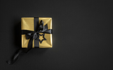 Banner with gold gift box and black ribbon on a black background. Top view, copyspace.