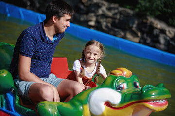 Dad and daughter on a crocodile inflatable boat in a summer amusement park.