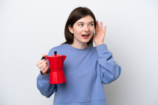 Young Russian woman holding coffee pot isolated on white background listening to something by putting hand on the ear