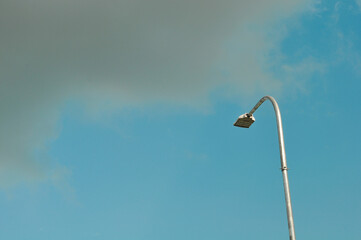 A TURNED OFF STREET LIGHT AND BLACK CLOUD IN BLUE SKY BACKGROUND 
