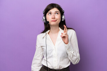 Telemarketer Russian woman working with a headset isolated on purple background with fingers crossing and wishing the best