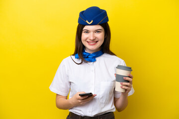 Airplane stewardess Russian woman isolated on yellow background holding coffee to take away and a mobile