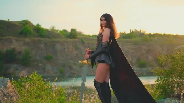 Fantasy woman viking princess warrior. Warlike girl Amazon. Lady nordic style sexy valkyrie goddess holding sword in hand. Leather costume armor cloak flies in wind. Mountains sunset sky nature summer