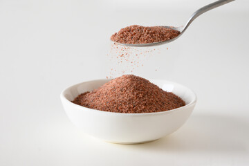 Pouring Indian Black salt Kala namak in bowl on white background. Close up. Useful for vegetarians as a source of iron.