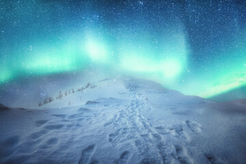 Aurora borealis over snowy hill with footprint and snowing on the peak of mountain in winter