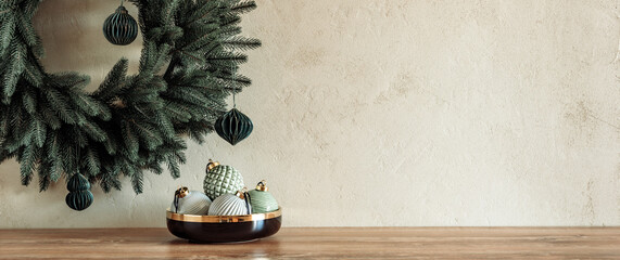 Minimal composition with pastel colored baubles in bowl on table with Christmas wreath on textured...