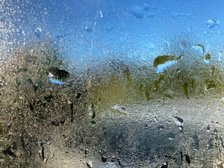 a steamed up window with dewdrops in front of nature background and blue sky