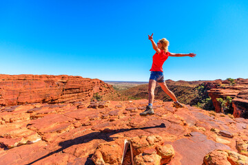 Young hiking girl jumping at Kings Canyon. Enjoying in Red Center Outback. Jumper among sandstone...