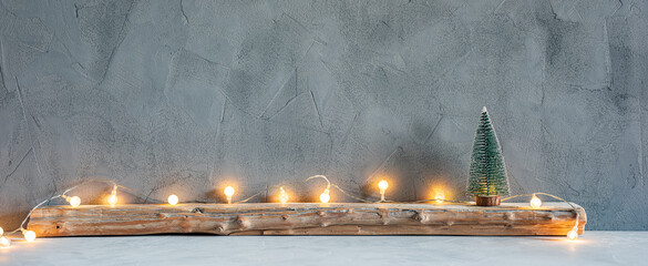 Small Christmas tree with lights on an old wooden plank on a textured gray stone wall background