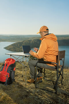 man sitting in chair near autumn lake and working online using laptop. freedom, work remote.