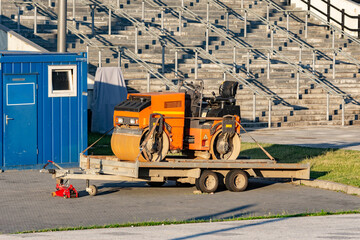 Small orange road roller parked on a a trailer after work