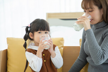 Happy asian family Mom and daughter drink milk at home .