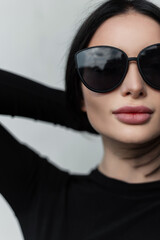 Female urban close-up portrait of a beautiful woman with sexy lips with black trendy sunglasses in trendy black clothes straightens her hair on a gray background in the city. Half of a woman's face