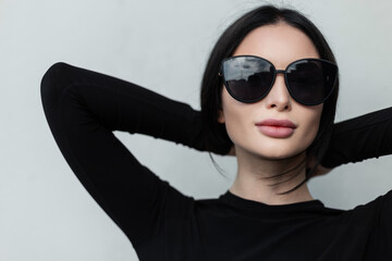 Urban fashion female portrait of pretty woman with sexy lips with stylish black fashionable sunglasses in black trendy outfit on a gray background