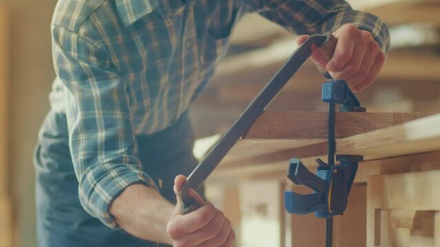 Close-up of a Young Artisan Craftsman in a Checkered Shirt, and Protective Glasses Using a Hand Scraper to Remove the Bark from the Wood Bar. Woodworking. Hands with a Sharp Knife. Wood Knife