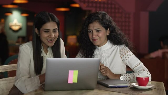 Enticing two Indian female friends supporting different team on laptop.young Asian women siting on upset with loser video game scored and other female wining at the coffee shop.