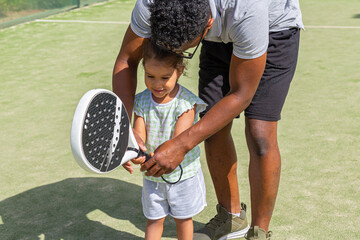 Black father teaching daughter to play paddle tennis 