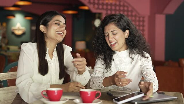  two Indian female friends of group supporting different team on laptop excited  young Asian women siting on upset with loser football game scored and other girl wining at the coffee shop.
