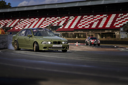 12-05-2022 Riga, Latvia A Green Car Driving Down A Race Track With A Person Watching From The Side Of The Track Behind It.