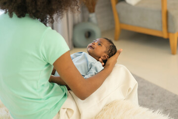 Young mother African American holding her one-month-old newborn baby son carefully and gently in bedroom. Adorable little infant sleep well in warm embrace of motherhood. Happy mother's day concept