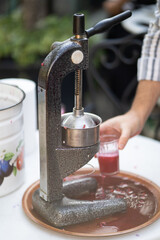 Close up process of squeezing pomegranate using manual mechanical juicer to obtain useful vitamins from natural product. Hands of seller from farmers market who extrude fresh fruit juice into glass
