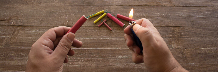 Image of the hands of a man who lights the fuse of a firecracker with a lighter. Reference you have celebrations and the danger of the barrels. Horizontal banner 
 - obrazy, fototapety, plakaty