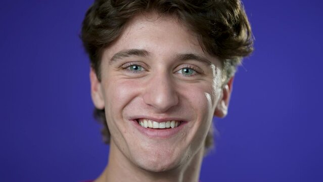 Slow motion closeup portrait of smiling happy young hipster man 20s isolated on solid purple background with copy space in studio