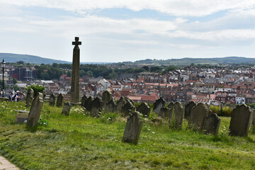 Row of gravestone and  gravestone cross  on the hill background with Whitby town surround  green meadow and white flower bloom in summer