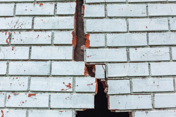Building Exterior Wall Cracked Damaged red bricks blue paint structure dangers closeup photograph.