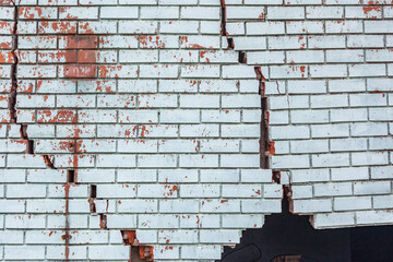 Building Exterior Wall Cracked Damaged red bricks blue paint structure dangers closeup photograph.