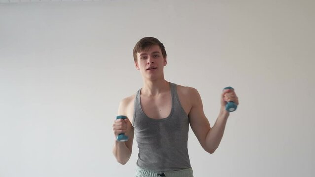 Enjoying sport. Funny man. Ridiculous dance. Happy funky guy in sweaty vest playing fool with dumbbells in hands posing light gray background.