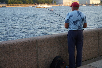 Saint Petersburg, Russia - August 19, 2022: A fisherman with a fishing rod on the embankment of the river Neva St. Petersburg