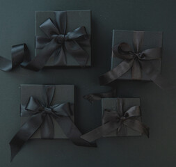Black Friday sales concept. Four gift box with black satin ribbon on black background, top view.