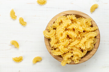 Dried macaroni cockerel scallops. Pasta in a wooden bowl and on a white table.