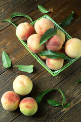 Ripe peaches in a basket on a wooden table with scattered leaves.