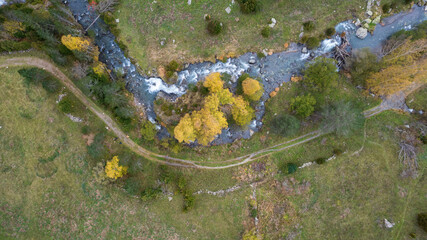 Aerial view over small river in pyrenees whit yellow and green trees 