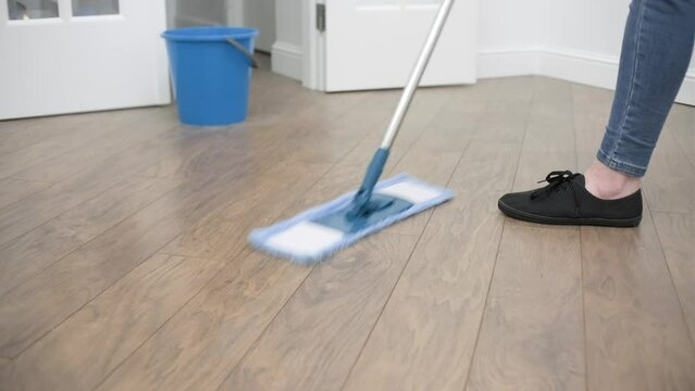 Woman in casual clothes cleaning wooden laminate floor using microfiber wet mop pad, doing homework cleaning routine. Housekeeping job. Cropped close up