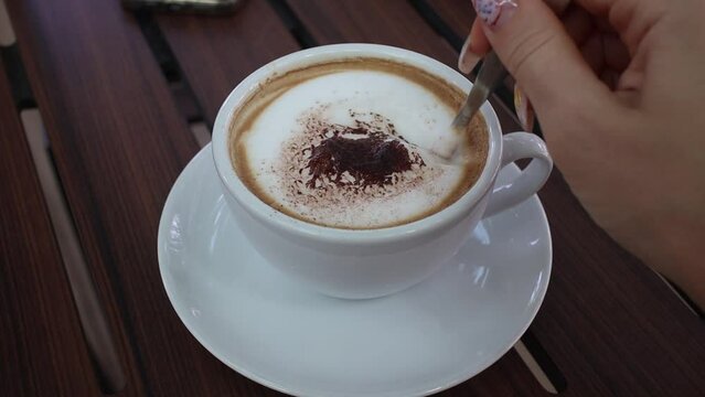 Woman's hand stirs cappuccino coffee with a spoon