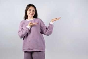 Beautiful brunette woman in comfortable muslin pajamas of lavender color shows her hands to the place for text - obrazy, fototapety, plakaty