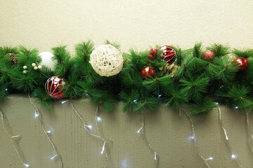 New Year's garland with Christmas toys and lights lies on a gray curb against a beige wall.
