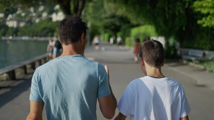 Parent giving life advice to teenager kid. Back of father and son walking together outside in park city. Dad talking to boy. manhood concept - Powered by Adobe