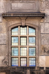 Rectangular cellular arched window with opaque glass against the background of an old weathered stone wall of brown color. From the Windows of the world series.