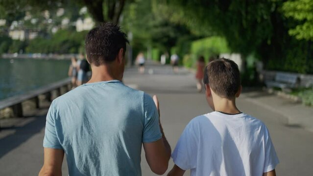 Parent giving life advice to teenager kid. Back of father and son walking together outside in park city. Dad talking to boy. manhood concept