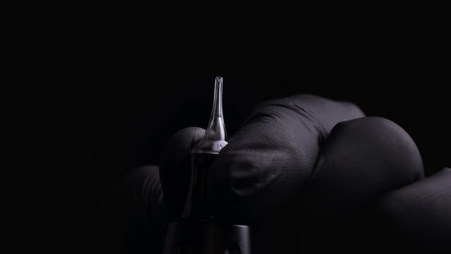 Hands of a master of permanent make-up of eyebrows, lips and eyelashes in black sterile gloves. With macro shot of installing a cartridge for permanent makeup in a tattoo machine and snapping the lock