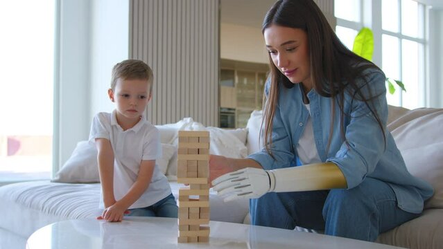 Mother plays jenga removing wooden block from tower gently by modern prosthetic hand