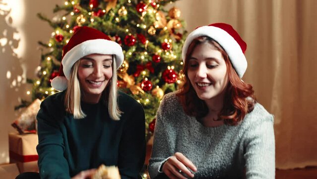 Two girls are eating the Christmas sweet Italian Panettone against the tree