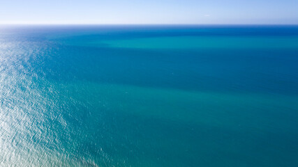 Fototapeta na wymiar Aerial view of the blue waters of the Mediterranean Sea and specifically of the Tyrrhenian Sea. Sunlight is reflected on the surface of the water. The sky, without clouds, is on background.