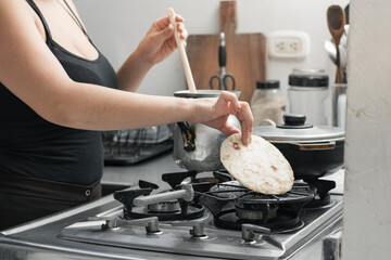 latina woman preparing a typical colombian breakfast, grabbing the arepa to turn it over while...